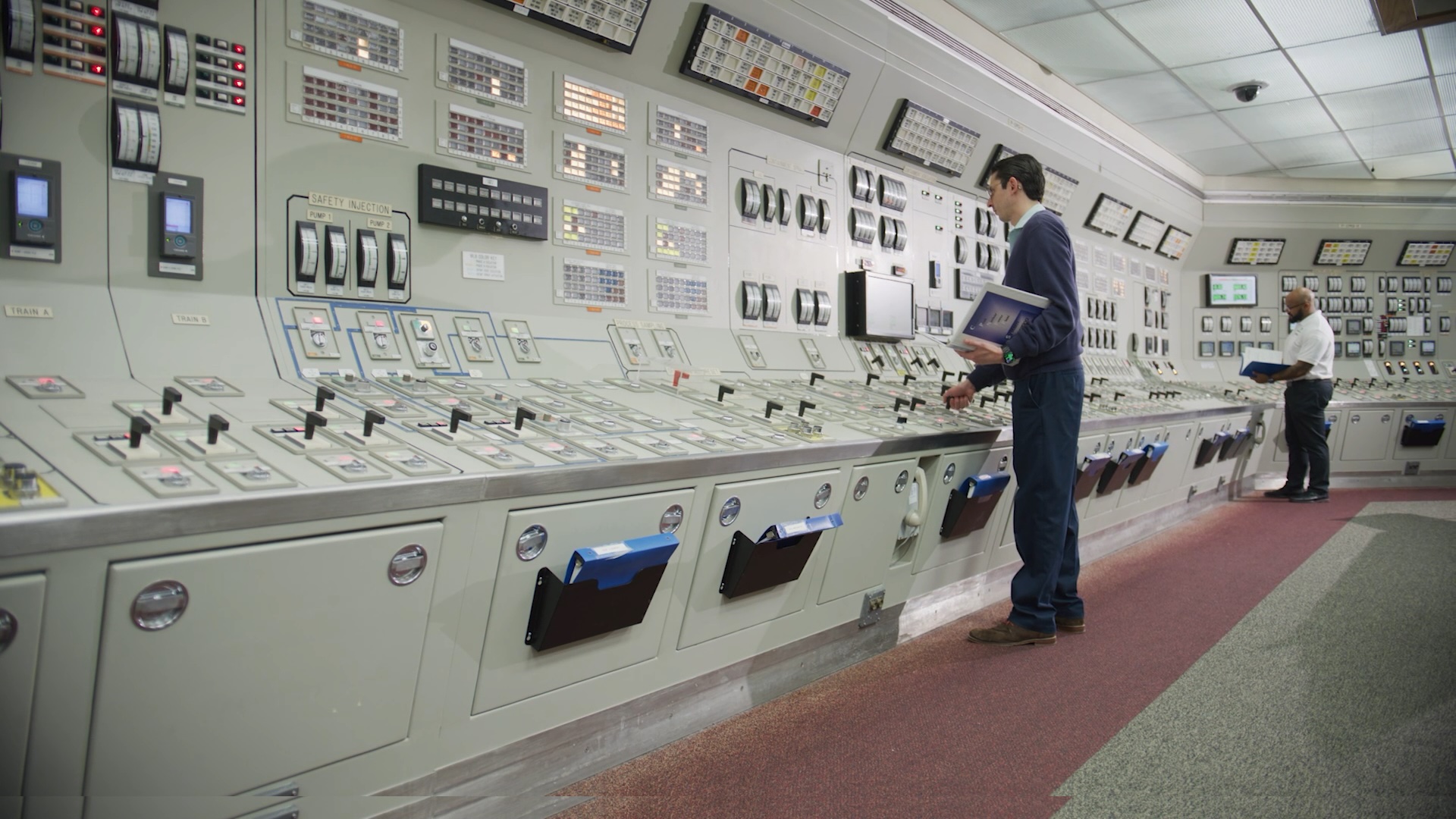 Operator monitoring digital screens alongside traditional analog control panels in a nuclear power plant control room.